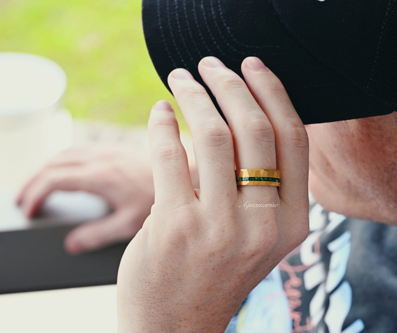 K&ouml;nnte beinhalten: Ein goldener Ring mit geh&auml;mmerter Oberfl&auml;che und einer Reihe gr&uuml;ner Edelsteine.