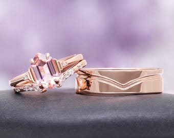 May include: Rose gold engagement ring set. The main ring features a large, light pink gemstone, complemented by smaller accent stones. The set includes a matching band with a V-shaped design. The rings are on a dark grey surface against a blurred purple background.