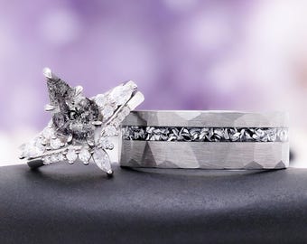 May include: A ring set featuring a pear-shaped salt and pepper diamond engagement ring with a cluster of small white accent stones, paired with a wide, hammered silver-tone band containing a central inlay of dark, textured metallic fragments.