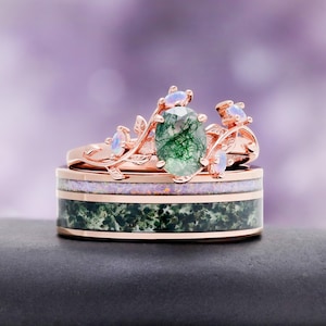 May include: A rose gold ring set featuring a band with a green moss agate inlay and a thin purple opal stripe, topped with a branch-like ring containing a central oval moss agate stone and four small round iridescent opal accent stones.