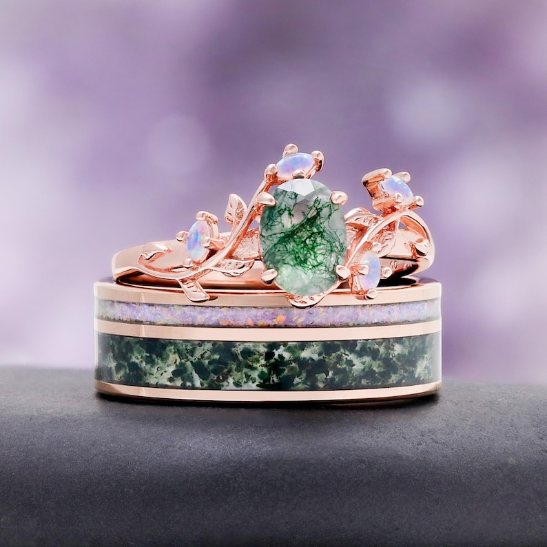 May include: A rose gold ring set featuring a band with a green moss agate inlay and a thin purple opal stripe, topped with a branch-like ring containing a central oval moss agate stone and four small round iridescent opal accent stones.