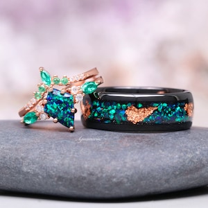 May include: A set of two rings, one with a large green and blue opal stone and emerald accents, and the other with a black band with green and gold glitter.