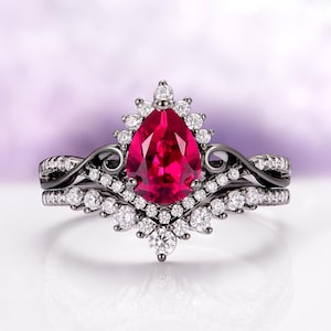 May include: A black engagement ring set with a pear-shaped, vibrant red gemstone as the centerpiece. The ring is surrounded by smaller, clear gemstones and features a matching band, creating a striking contrast against the black metal.