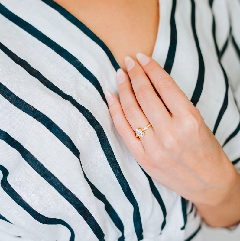 Puede incluir: Primer plano de una mano con un anillo de oro con un gran diamante de forma ovalada. El anillo est&aacute; engastado en una banda retorcida.