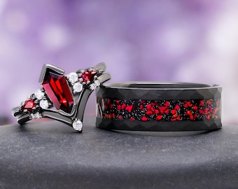 May include: A set of two black metal rings. One ring features a central kite-shaped red gemstone flanked by smaller red stones and clear round accent stones. The second ring is a wide band with a hammered texture and a central inlay of red fragments.