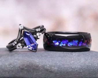 Puede incluir: Un juego de anillos de boda negro con una piedra preciosa azul y una banda negra con destellos iridiscentes de color púrpura y azul.