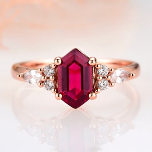 May include: A rose gold ring with a large, octagon-shaped ruby gemstone surrounded by smaller, round white gemstones.