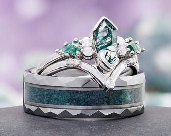 May include: A set of three rings, including a wedding band and two engagement rings. The engagement rings feature a large, clear, green-veined stone and smaller green and clear stones. The wedding band has a textured, dark gray exterior and a teal-colored interior.