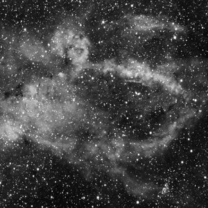 May include: A black and white photograph of a nebula in space. The nebula is a large, swirling cloud of gas and dust that is illuminated by nearby stars. The nebula is surrounded by a field of stars.