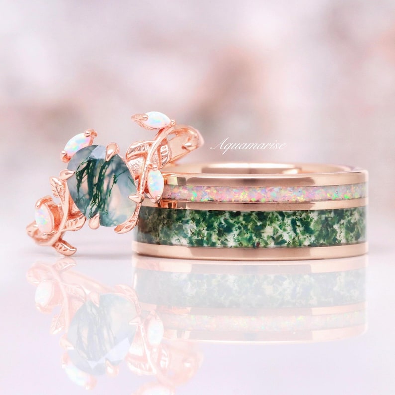 May include: A rose gold ring set featuring a band with a moss agate inlay and an opal inlay, paired with a leaf-shaped ring set with a central moss agate stone and small opal accents. The text Aquamarise is visible in the background.
