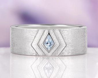 Könnte beinhalten: Ein silberner Ring mit strukturiertem Band und geometrischem Design. Der Ring hat einen hellblauen, rautenförmigen Edelstein in der Mitte. Der Ring wird auf einer reflektierenden Oberfläche präsentiert.