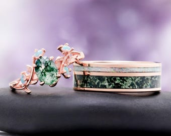 May include: A rose gold ring featuring an oval moss agate stone and small opal accents alongside a rose gold band inlaid with a horizontal strip of white opal above a wider band of dark green moss agate with a polished metallic finish.