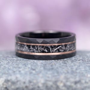 May include: A black tungsten carbide ring with a rose gold inlay and a meteorite inlay. The ring has a diamond-cut finish.