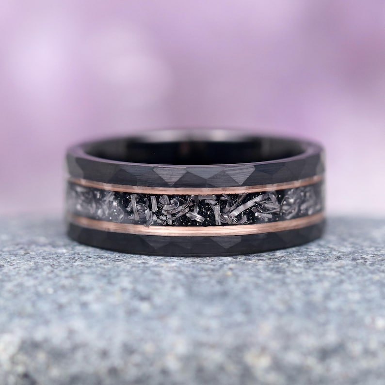 May include: A black tungsten carbide ring with a rose gold inlay and a meteorite inlay. The ring has a diamond-cut finish.