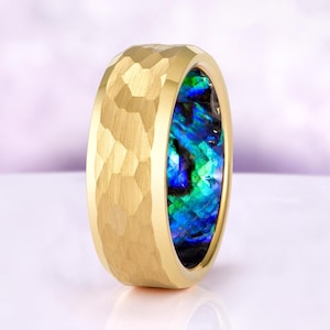 May include: A gold-colored ring with a textured, geometric pattern on the exterior. The interior of the ring features a vibrant, iridescent inlay of blue, green, and black. The ring is a close-up shot, showcasing the details of the jewelry.