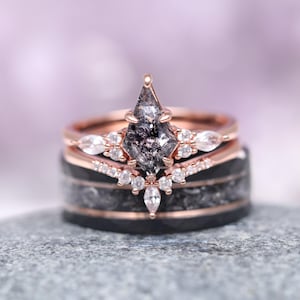 May include: A rose gold engagement ring set with a black diamond and a halo of smaller diamonds. The ring is set on a black band with a rose gold accent.