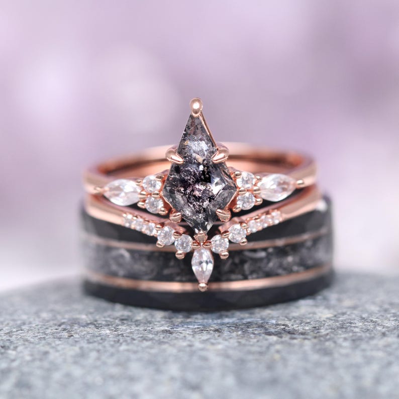 May include: A rose gold engagement ring set with a black diamond and a halo of smaller diamonds. The ring is set on a black band with a rose gold accent.