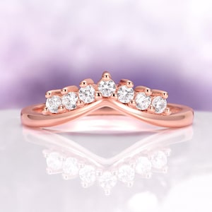 Könnte beinhalten: Roségoldener Ring mit geschwungenem Design, besetzt mit sieben runden, klaren Edelsteinen. Das Band des Rings hat eine glatte, polierte Oberfläche. Die Edelsteine sind gleichmäßig verteilt.