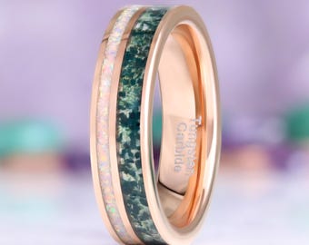 May include: A rose gold-toned ring featuring a polished metal band with two distinct inlays. One inlay consists of a white iridescent crushed material, while the other is a dark green textured stone. The interior is engraved with Tungsten Carbide.