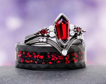 May include: A set of two rings. The top ring is black with a large, red gemstone and smaller white and red stones. The bottom ring is black with a red and black speckled inlay. The rings are displayed on a gray surface.