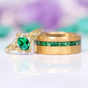 K&ouml;nnte beinhalten: Ein Paar goldene Eheringe mit einem gr&uuml;nen Edelstein. Der Verlobungsring hat einen gro&szlig;en ovalen gr&uuml;nen Edelstein, der von kleineren Diamanten umgeben ist. Der Ehering hat eine gr&uuml;ne Edelsteineinlage.