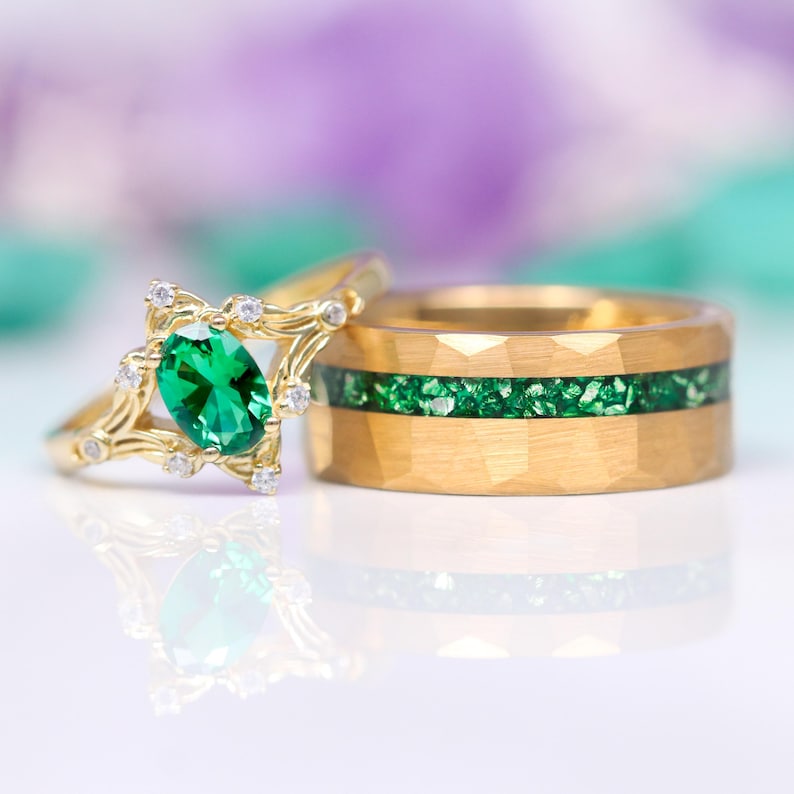 K&ouml;nnte beinhalten: Ein Paar goldene Eheringe mit einem gr&uuml;nen Edelstein. Der Verlobungsring hat einen gro&szlig;en ovalen gr&uuml;nen Edelstein, der von kleineren Diamanten umgeben ist. Der Ehering hat eine gr&uuml;ne Edelsteineinlage.