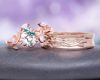 May include: Two rose gold rings. One ring features a central oval-shaped stone with green and white patterns, surrounded by small opalescent stones and leaf-like details. The other ring has a band with an engraved floral design.