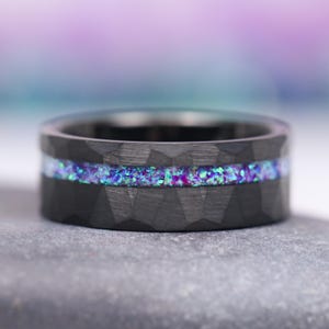 May include: A black tungsten carbide ring with a hammered finish and a thin band of iridescent purple and blue glitter.