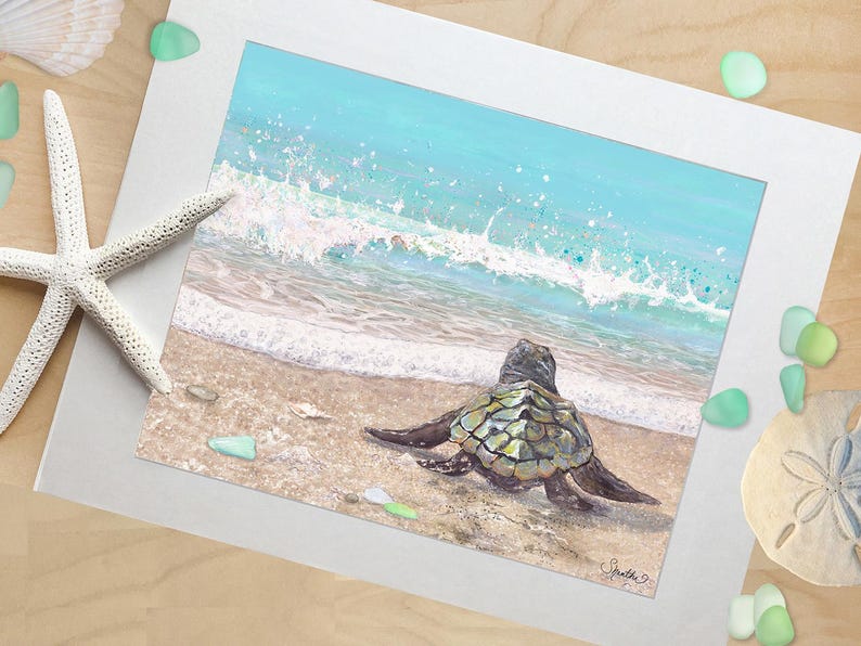 May include: A framed print of a sea turtle on a sandy beach, with a turquoise ocean and white waves in the background. The artwork is surrounded by a white mat, with a starfish and sea glass accents.