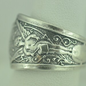 May include: Silver ring with an intricate design featuring a winged figure and floral motifs.