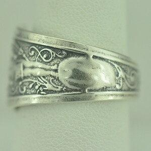 May include: Silver ring with an ornate design featuring a floral pattern and a smooth, oval-shaped center.