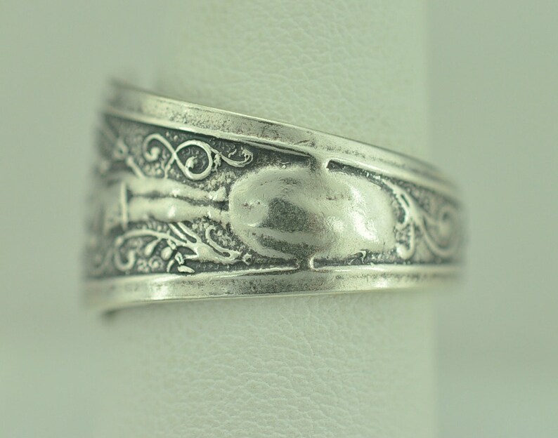 May include: Silver ring with an ornate design featuring a floral pattern and a smooth, oval-shaped center.