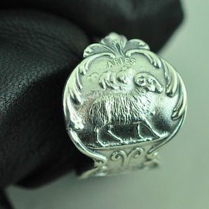 May include: A silver-toned Aries ring with a detailed ram illustration. The ring features the word "ARIES" at the top, and the ram is centered within a decorative border. The ring is shown against a dark background.