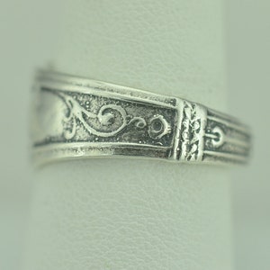 May include: Silver ring with a decorative floral design. The ring is made of sterling silver and has a polished finish.