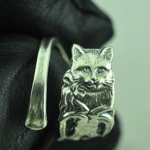 May include: A silver ring featuring a detailed cat design. The cat is seated with its head tilted and eyes closed. The ring is crafted from a thick band of silver.