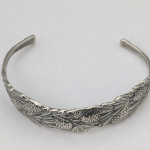 Pode incluir: Um bracelete de prata com um design de pinha.