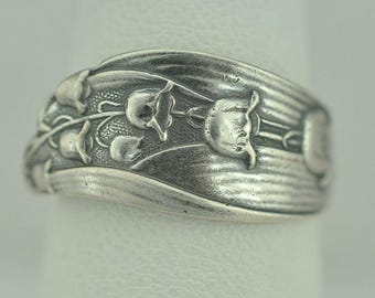 May include: A silver-toned ring featuring a raised, embossed floral pattern of lily of the valley flowers and elongated leaves. The metal surface has a darkened, oxidized finish in the recessed areas to highlight the intricate botanical details.