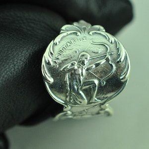 May include: Silver ring with a detailed design featuring the Sagittarius zodiac symbol, a centaur holding a bow and arrow, with the word "Sagittarius" inscribed around the design.