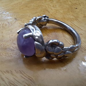 May include: A silver ring with a large, round, purple amethyst gemstone set in a floral design.