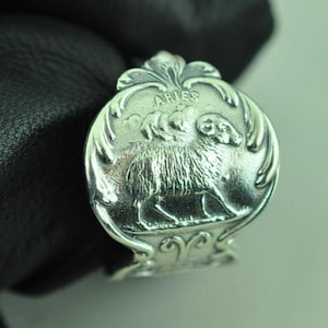 May include: A silver-toned metal ring featuring a raised relief design of a ram, representing the Aries zodiac sign. The word ARIES is embossed above the ram, surrounded by decorative scrollwork details on the circular face of the ring.