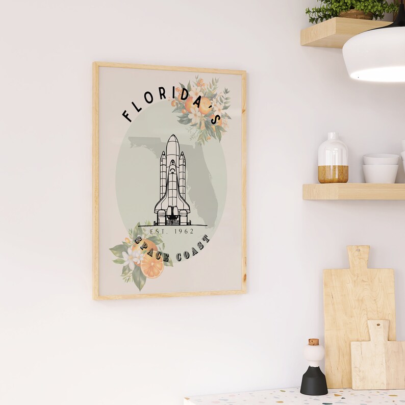 May include: A framed print featuring a space shuttle illustration with the text "Florida's Space Coast Est. 1962." The design includes floral accents and a map outline of Florida, set against a neutral background.