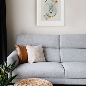 May include: A framed print featuring a Florida Space Coast design. The artwork includes a stylized illustration of a space shuttle, floral accents, and the text "Florida Space Coast." The print is displayed above a gray sofa with decorative pillows.
