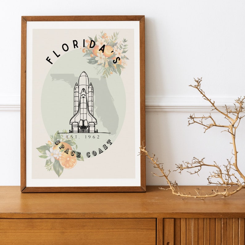 May include: A framed art print featuring a black and white illustration of a space shuttle, with the text "Florida's Space Coast" and "Est. 1962". The design includes floral accents and a map outline of Florida.
