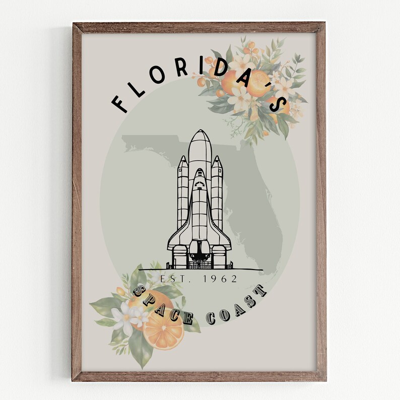 May include: A framed art print featuring a black and white illustration of a space shuttle, with the text "Florida's Space Coast Est. 1962." The design includes orange blossoms and oranges, set against a light green background and a wooden frame.