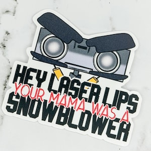 May include: A white sticker with a black and gray cartoon robot with the text "Hey Laser Lips Your Mama Was A Snowblower" in black and red.