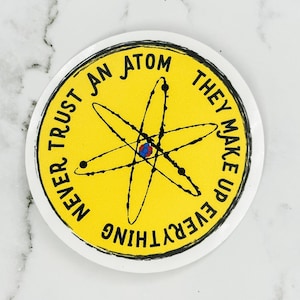 May include: Yellow round sticker with black text that reads "Never trust an atom they make up everything" and a black and white drawing of an atom in the center.