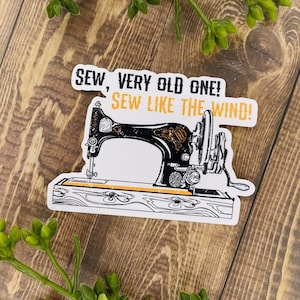 May include: A white sticker with a black and white illustration of an old sewing machine. The sticker has the text "Sew, very old one! Sew like the wind!" in black and orange.
