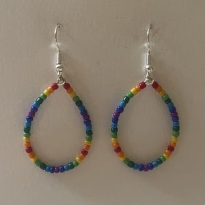 May include: A pair of teardrop-shaped earrings constructed from small, multicolored glass beads arranged in a rainbow pattern. Each earring features a silver-toned metal hook for attachment, creating a simple, open-loop design with vibrant hues.