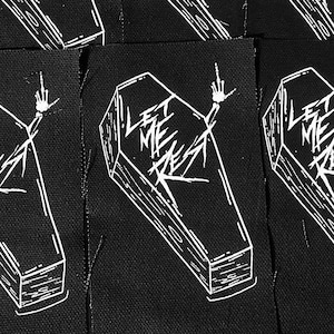 May include: Eight black fabric patches featuring white embroidered coffins with the words "Let Me Rest" in a stylised font. Each coffin has a hand sticking out of it with the middle finger extended.