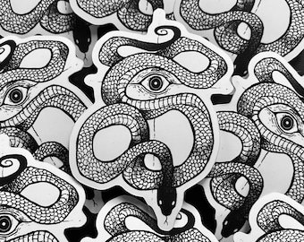 Op de afbeelding: Een verzameling zwart-witte stickers met een gedetailleerde illustratie van een slang met een oog in het midden. De slang is opgerold, met ingewikkelde schubbenpatronen en een gestileerd oog. De stickers staan op een witte achtergrond.